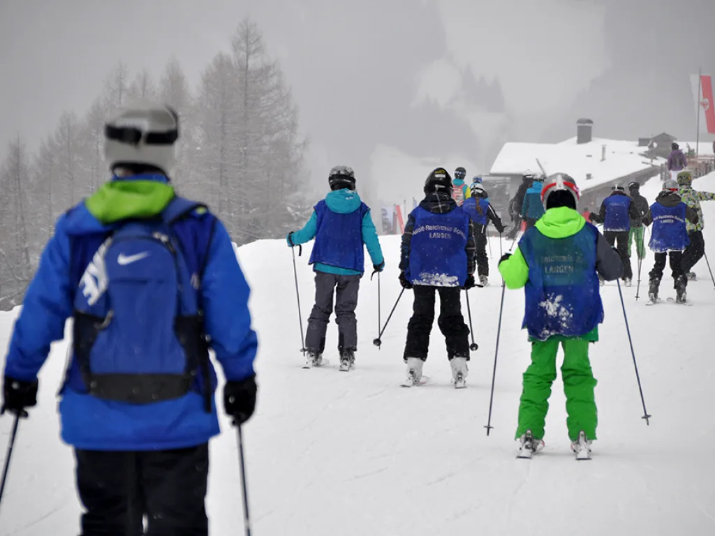 Gruppe geht bei Nebel auf Skiern zur Hütte.